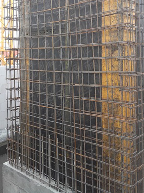 Zbrojenie pionowego elementu konstrukcyjnego z widoczną szalunką i siatką z prętów stalowych. Detal konstrukcji w trakcie budowy.