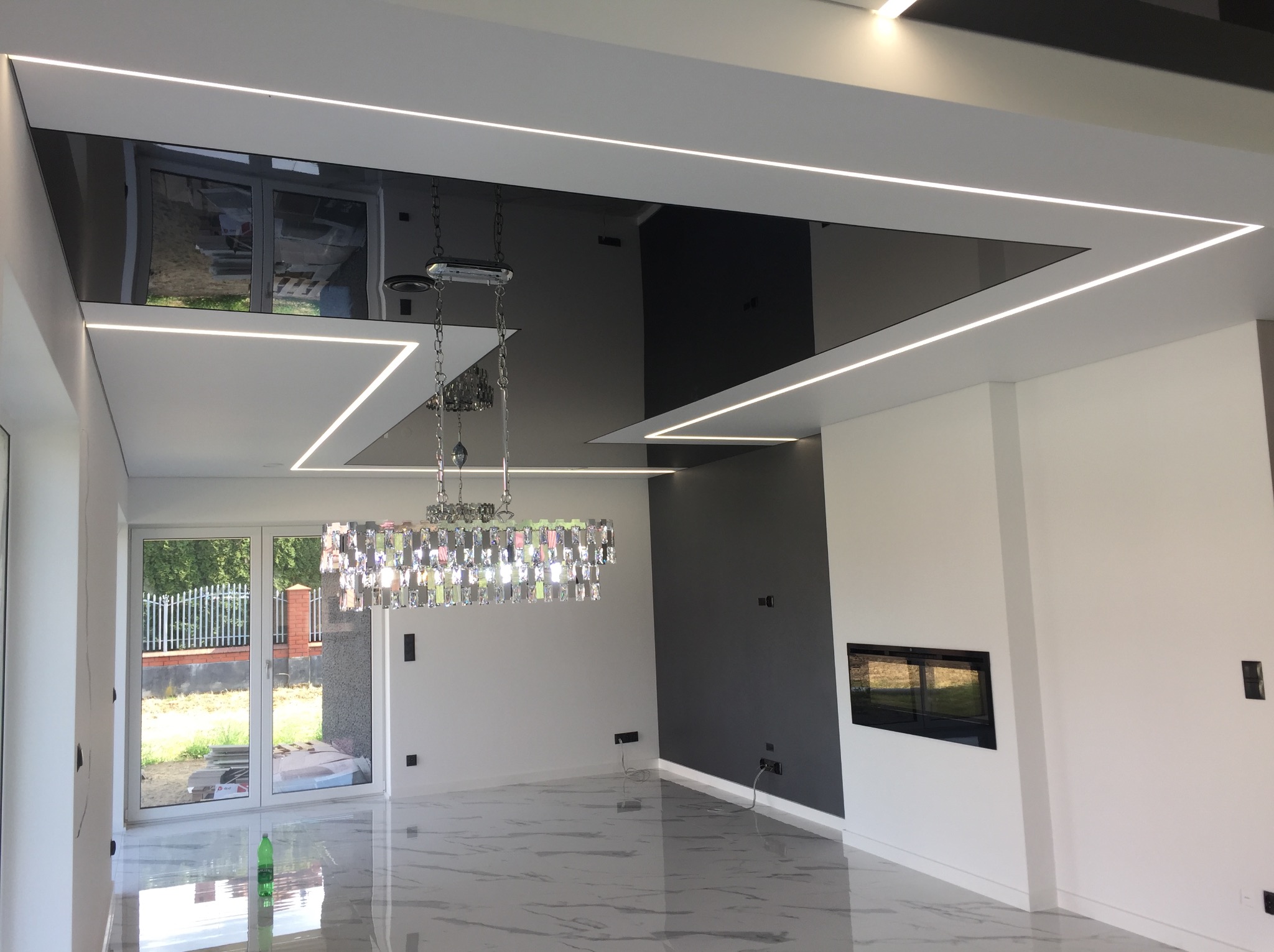 Nowoczesny salon z czarnym, lustrzanym sufitem podwieszanym i liniowym oświetleniem LED. Kryształowy żyrandol, marmurowa podłoga i kominek dodają elegancji.