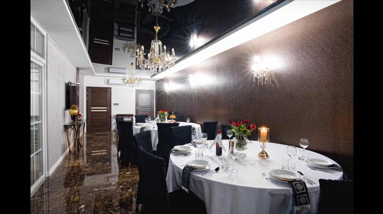 Eleganckie wnętrze sali bankietowej z błyszczącą podłogą i sufitem lustrzanym, oświetlone kryształowymi żyrandolami i kinkietami, z nakrytymi stołami gotowymi na przyjęcie.