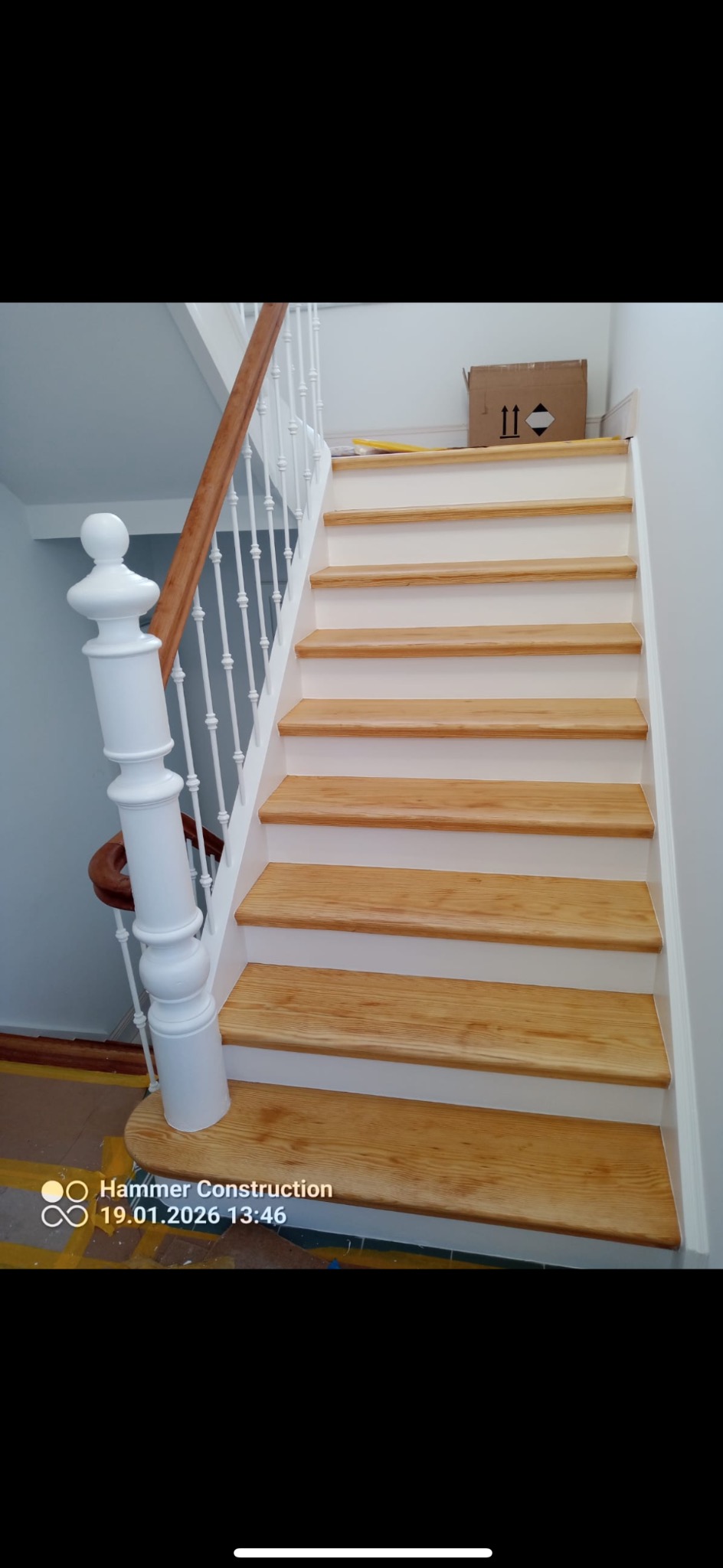 Odnowione schody drewniane z białymi podstopnicami i balustradą. Widoczne detale wykończenia i naturalne usłojenie drewna. Ujęcie z dołu, podkreślające estetykę.