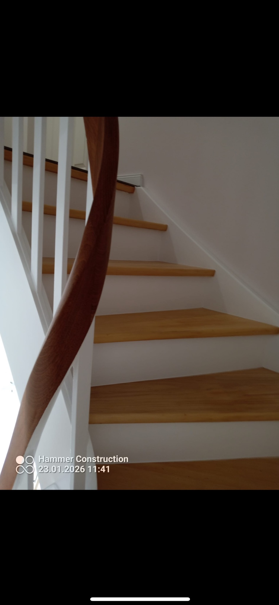 Drewniane schody z białymi podstopnicami i balustradą, widok z dołu, ukazujący detale wykończenia i naturalne usłojenie drewna.