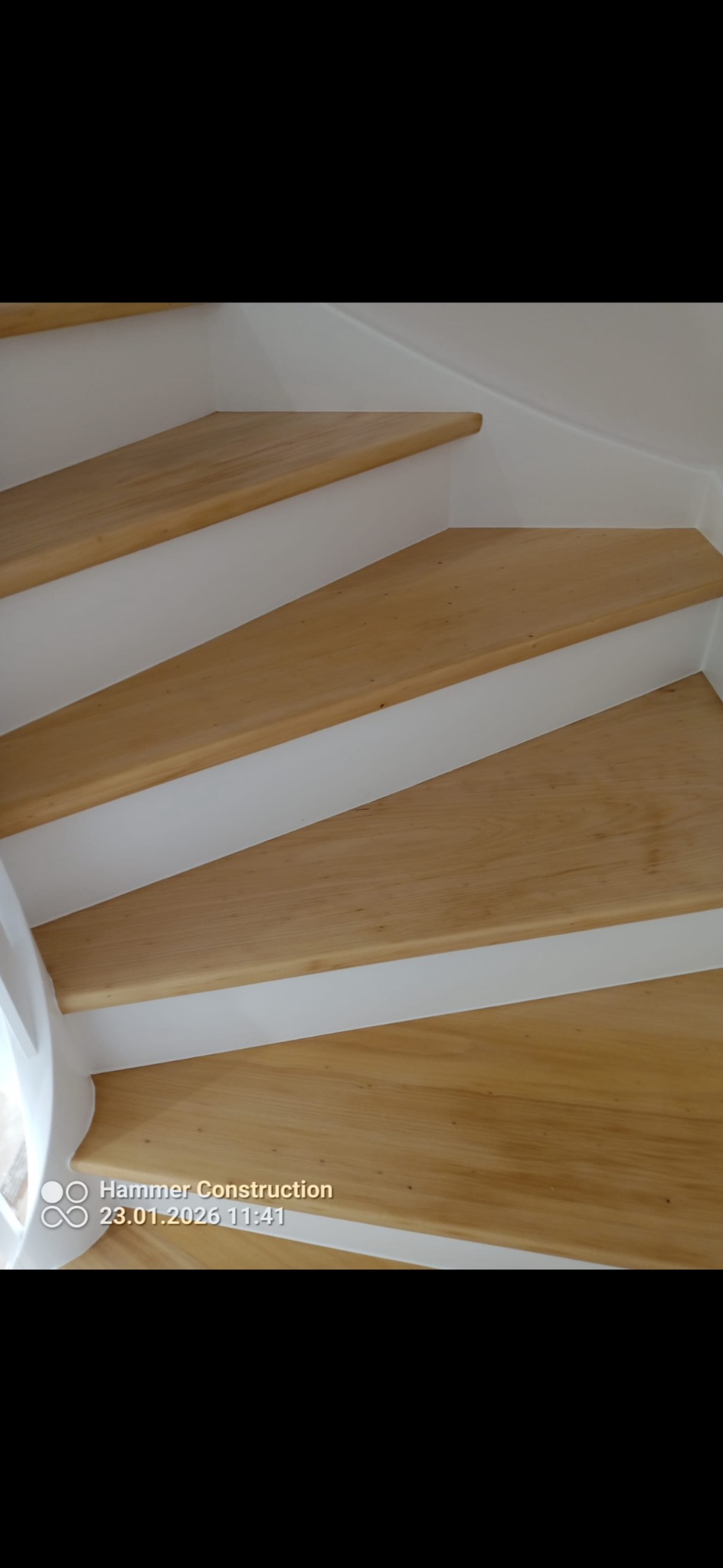 Jasne, drewniane schody z białymi podstopnicami, widok z góry, ukazujący precyzję wykonania i estetyczne wykończenie. Naturalne światło podkreśla strukturę drewna.