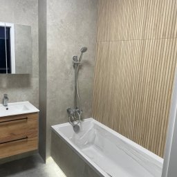SK&A-Technika Serhii Kushnir - Wykończona łazienka w Poznaniu: drewnopodobna ściana, wanna z baterią, umywalka z szafką i lustro. Nowoczesny design, szare płytki, minimalistyczny styl.