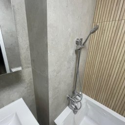 SK&A-Technika Serhii Kushnir - Nowoczesna łazienka z wanną i armaturą w odcieniach szarości, akcentowana drewnianą ścianą z pionowymi panelami. Minimalistyczny design, chromowana bateria.