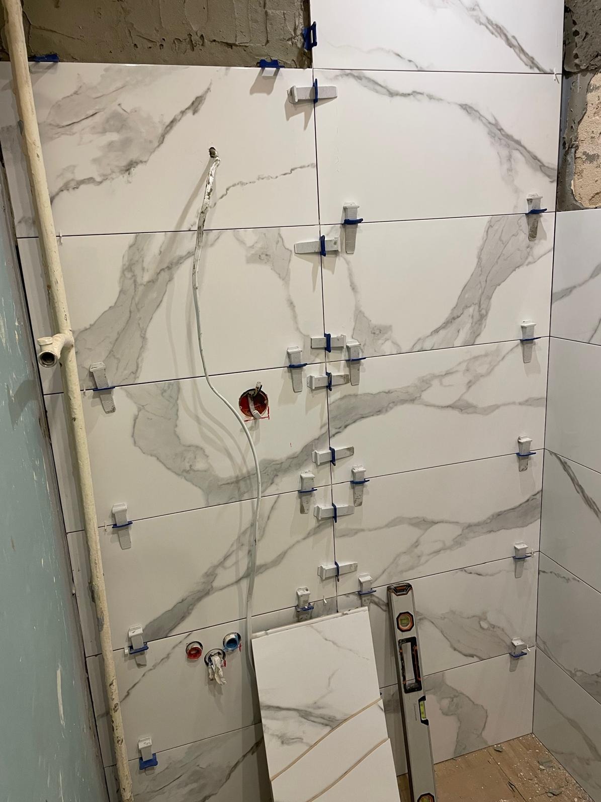 Ściana w trakcie układania płytek imitujących marmur, z użyciem krzyżyków dystansowych. Widoczne przewody elektryczne i poziomica.