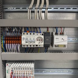 LuxSolutions - Rozdzielnica elektryczna z zamontowanymi bezpiecznikami, gniazdkiem i modułami WAGO, okablowana przewodami o różnych kolorach, w szarej obudowie.