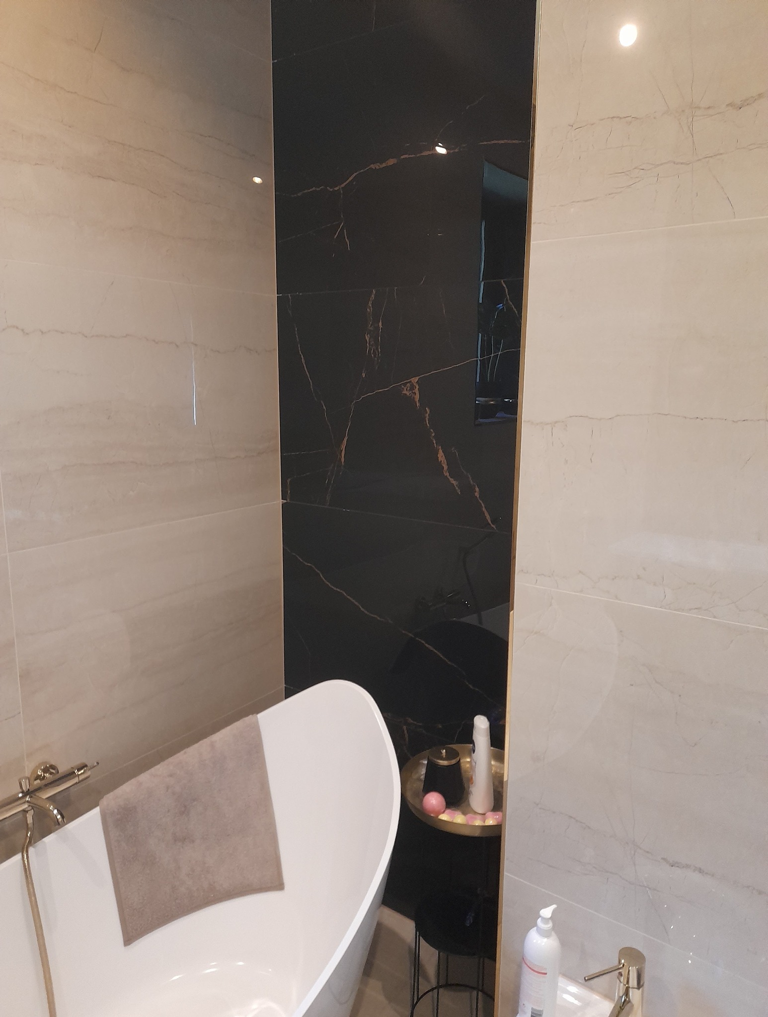 Elegancka łazienka z wolnostojącą wanną i marmurowymi płytkami w odcieniach beżu i czerni ze złotymi żyłami. Nowoczesny design z akcentami glamour.