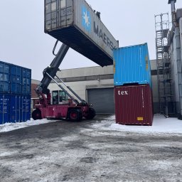 Northumberland GmbH - Wózek widłowy Ferrari 258 podnosi kontener Maersk na placu składowym. W tle budynek magazynowy i ustawione kontenery. Zimowa sceneria z resztkami śniegu.