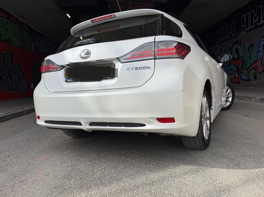 Biały Lexus CT200h, widok z tyłu, zaparkowany w tunelu z graffiti. Widoczne tylne światła, logo Lexus i oznaczenie modelu. Asfaltowa nawierzchnia, oświetlenie dzienne.