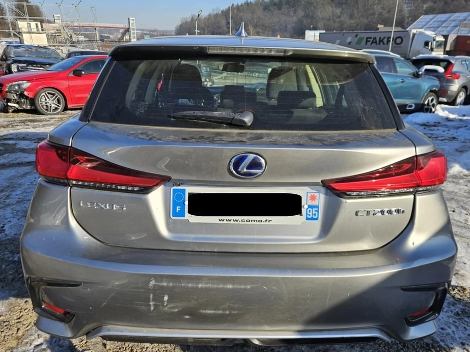 Tył szarego samochodu Lexus CT 200h z francuską tablicą rejestracyjną na tle parkingu i drzew. Widoczne zarysowania na karoserii.