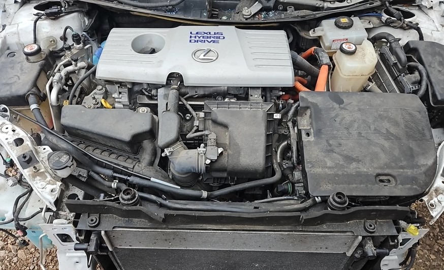 Otwarta maska Lexusa Hybrid Drive ukazuje silnik spalinowo-elektryczny, widoczne elementy układu chłodzenia i osprzęt silnika. Detaliczny widok na wnętrze komory silnikowej.