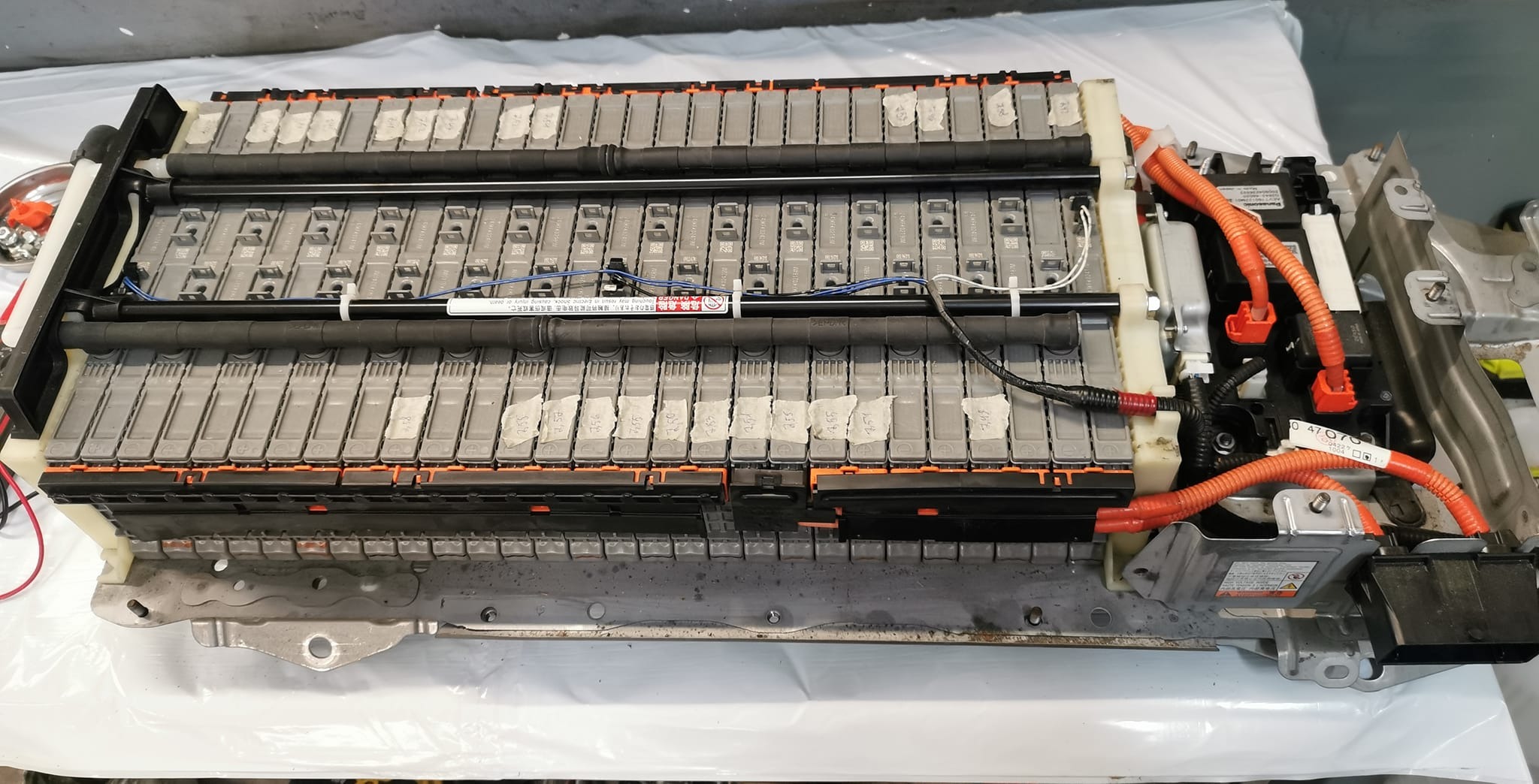 Otwarta obudowa akumulatora hybrydowego z widocznymi modułami, przewodami i elementami mocującymi. Widoczne oznaczenia na modułach. Praca warsztatowa.