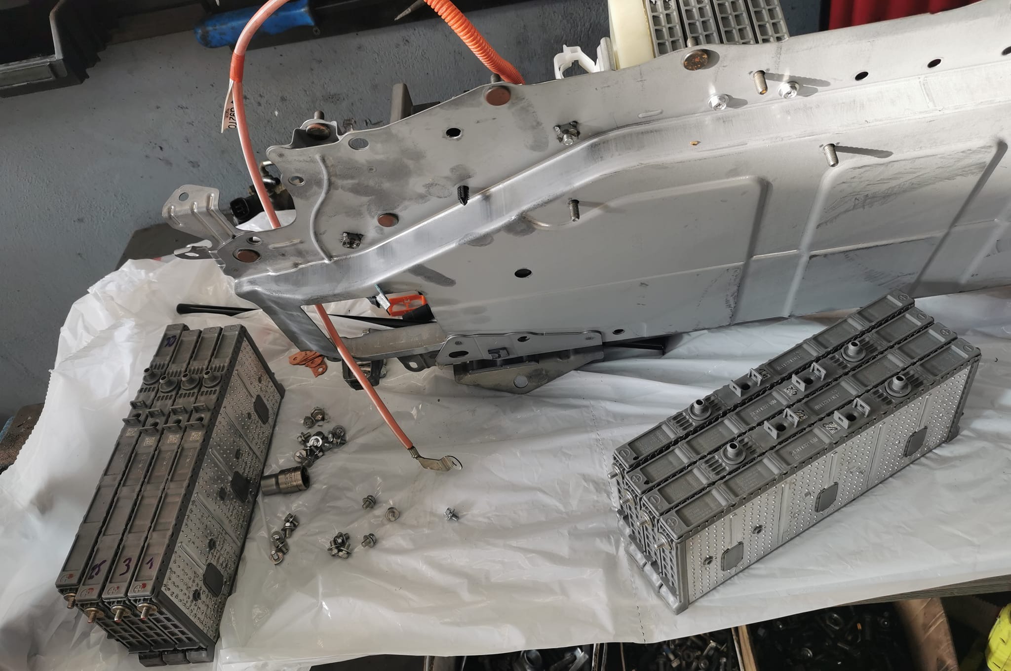 Rozłożony akumulator pojazdu elektrycznego z widocznymi modułami, przewodami i elementami konstrukcyjnymi na białym podłożu w warsztacie.