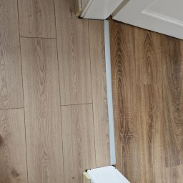 KK Studiokoloru - Połączenie jasnych i ciemnych paneli podłogowych z widoczną listwą progową w białej ościeżnicy drzwi, ukazujące precyzyjne wykończenie podłogi.