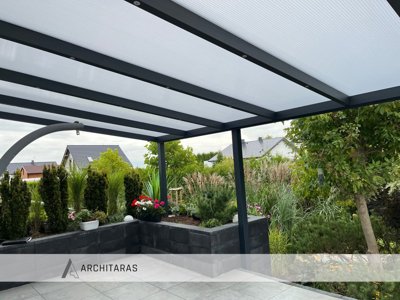 Nowoczesna pergola metalowa z białym zadaszeniem, otoczona zielenią i kwiatami. Widok na ogród z elementami małej architektury.