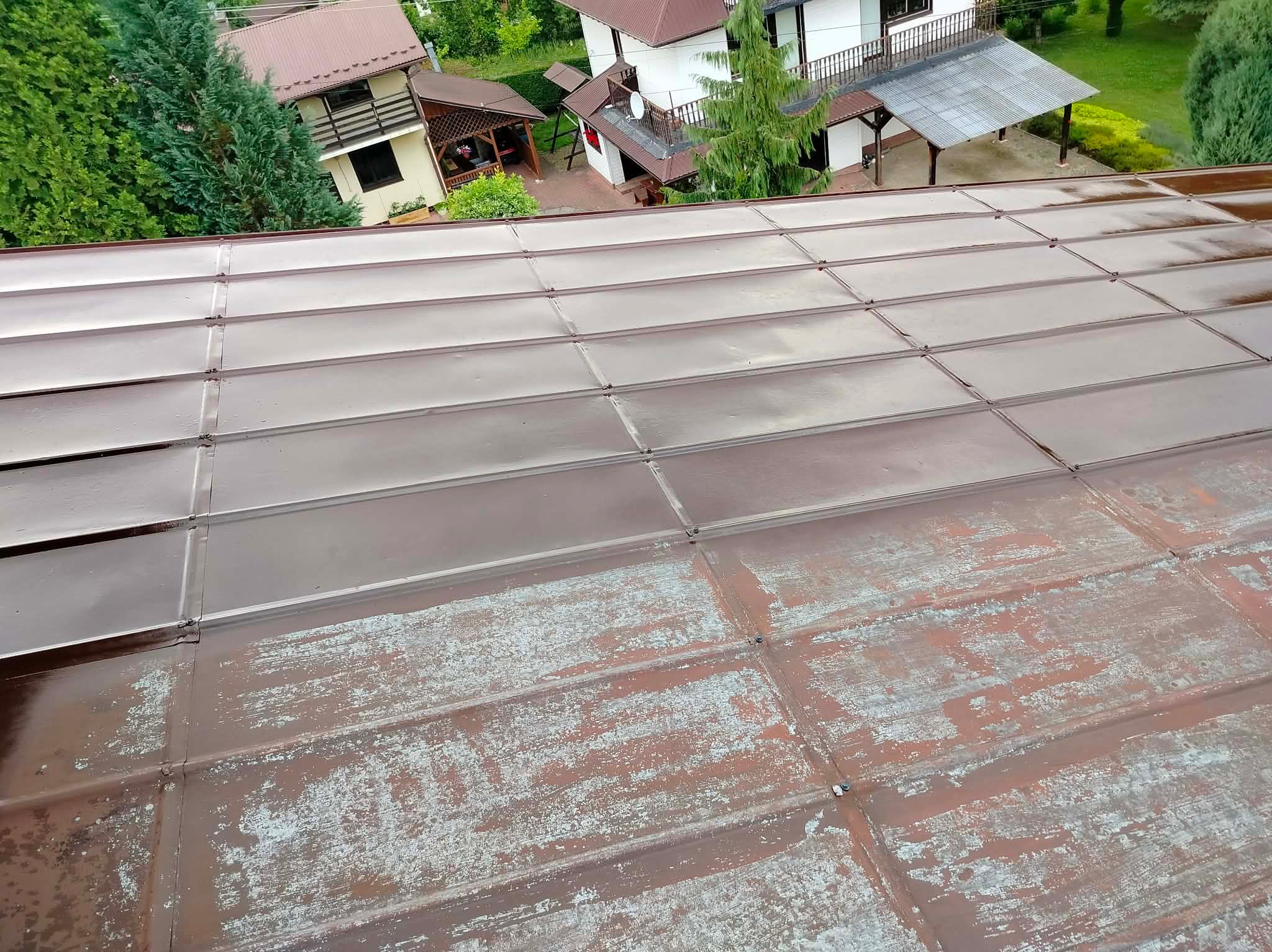 Częściowo odnowiony, brązowy dach z blachy trapezowej. Górna część dachu jest świeżo pomalowana, dolna z widocznymi śladami starej farby i korozji. Widok z góry.