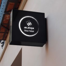 MaTaWi Marek Wojakowski - Kwadratowy, podświetlany szyld reklamowy 'Alanya Doner Kebab' na elewacji budynku, z widocznym fragmentem balkonu i lampy ulicznej w tle. Minimalistyczny design.