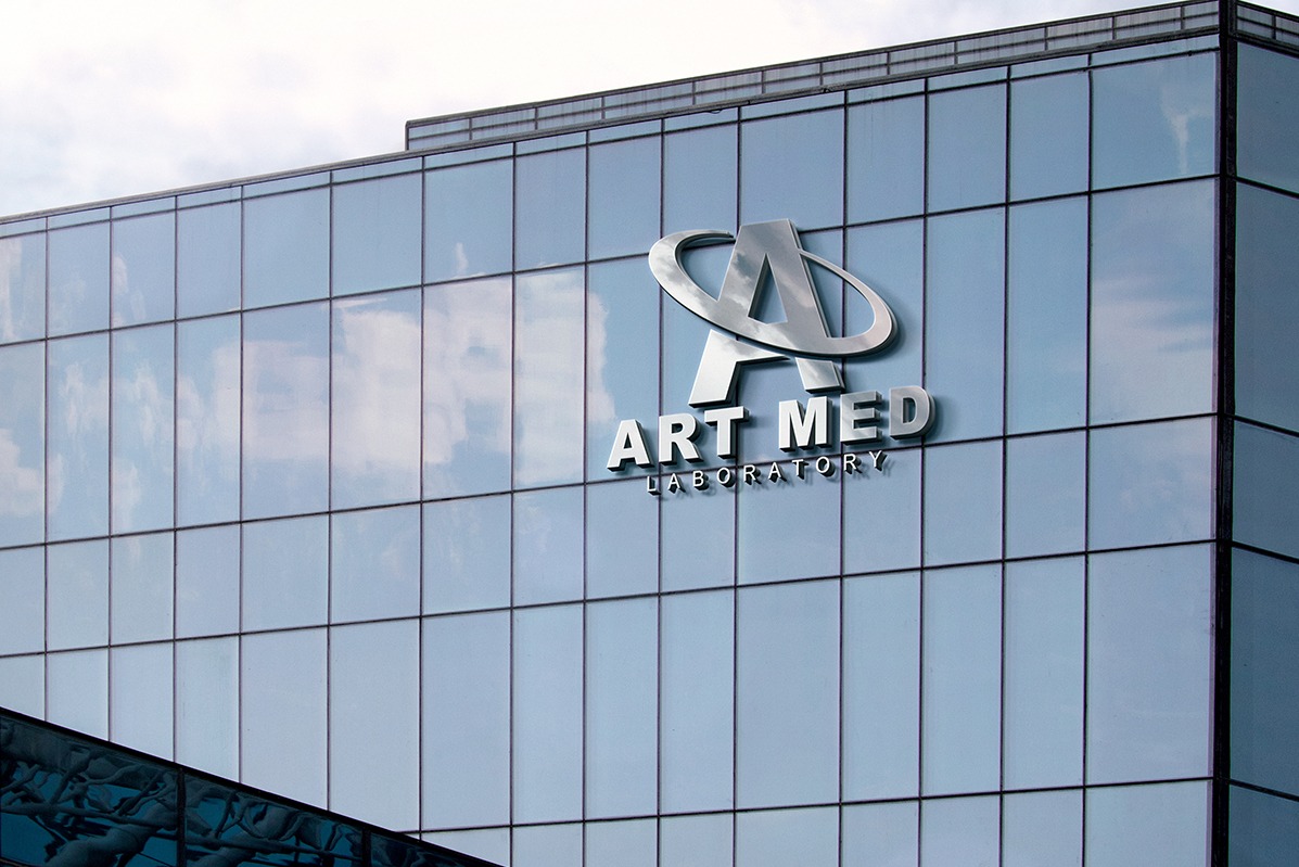 Elewacja budynku z logo 'ART MED Laboratory' w srebrnej kolorystyce, widoczne odbicie chmur w szklanej fasadzie. Ujęcie z dołu, podkreślające nowoczesny charakter.