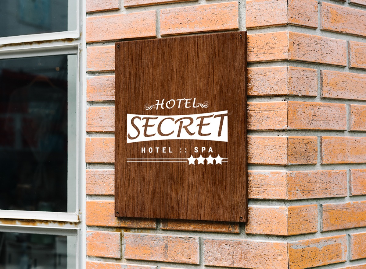 Drewniana tabliczka z logo 'Hotel Secret Hotel :: Spa' na ceglanej ścianie obok okna. Minimalistyczny design, ciepłe oświetlenie, wyraźna typografia.