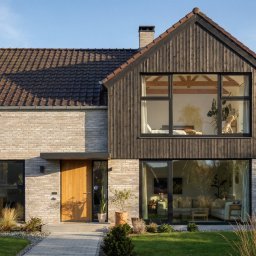 Follow River Sp. z o.o. - Nowoczesny dom z jasnej cegły i ciemnego drewna, duże okna, dwuspadowy dach z brązową dachówką, zadbany trawnik, kostka brukowa, minimalistyczny design.