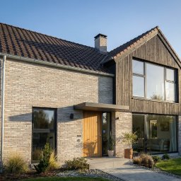 Follow River Sp. z o.o. - Nowoczesny dom jednorodzinny z cegły i drewna w Warszawie. Dwuspadowy dach z brązową dachówką, duże okna i minimalistyczne detale architektoniczne.