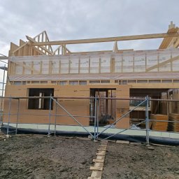 Follow River Sp. z o.o. - Budowa domu w technologii szkieletowej: widok na drewnianą konstrukcję ścian i dachu, zabezpieczoną folią, z widocznymi rusztowaniami i izolacją termiczną.