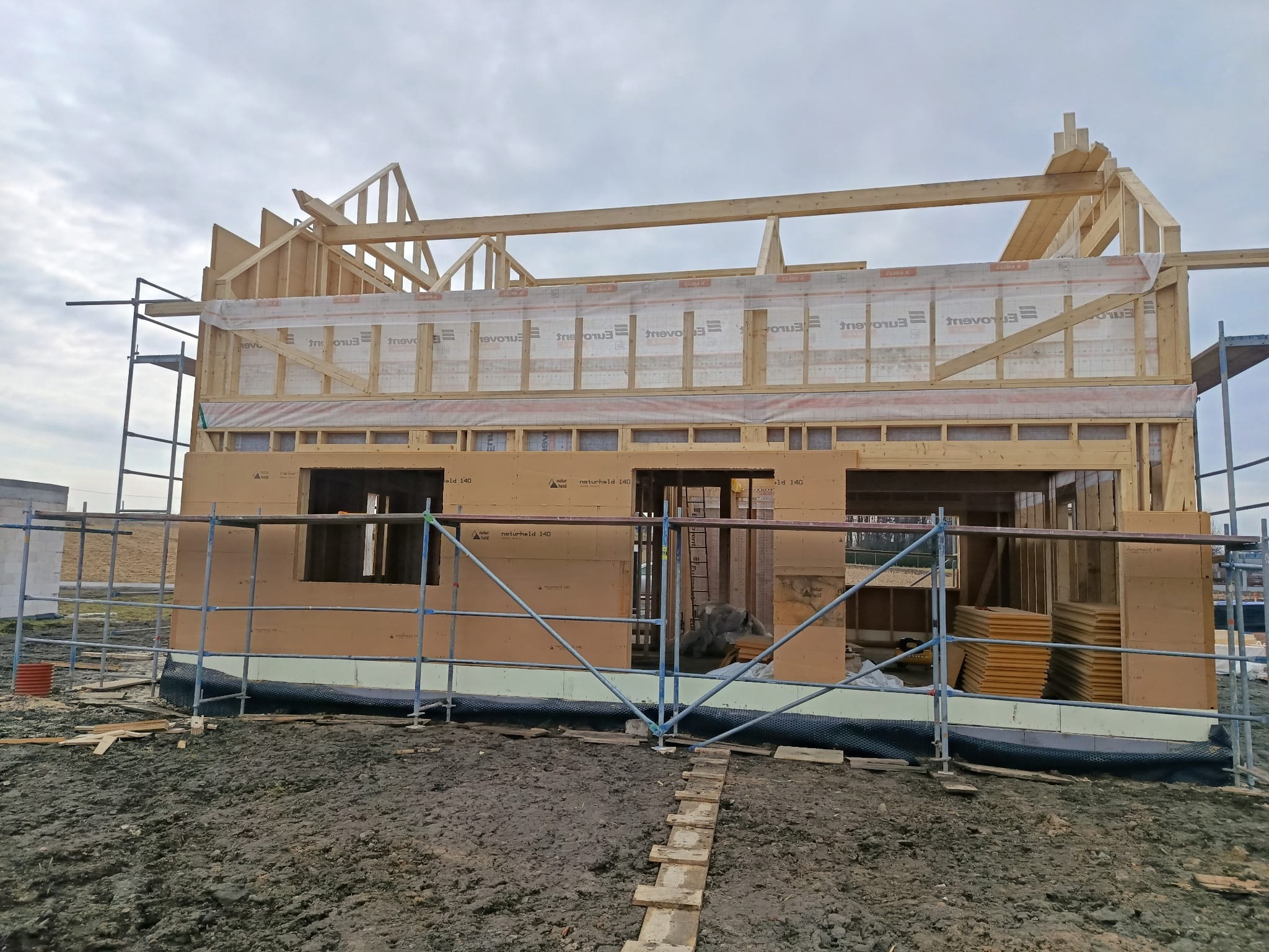 Budowa domu w technologii szkieletowej: widok na drewnianą konstrukcję ścian i dachu, zabezpieczoną folią, z widocznymi rusztowaniami i izolacją termiczną.