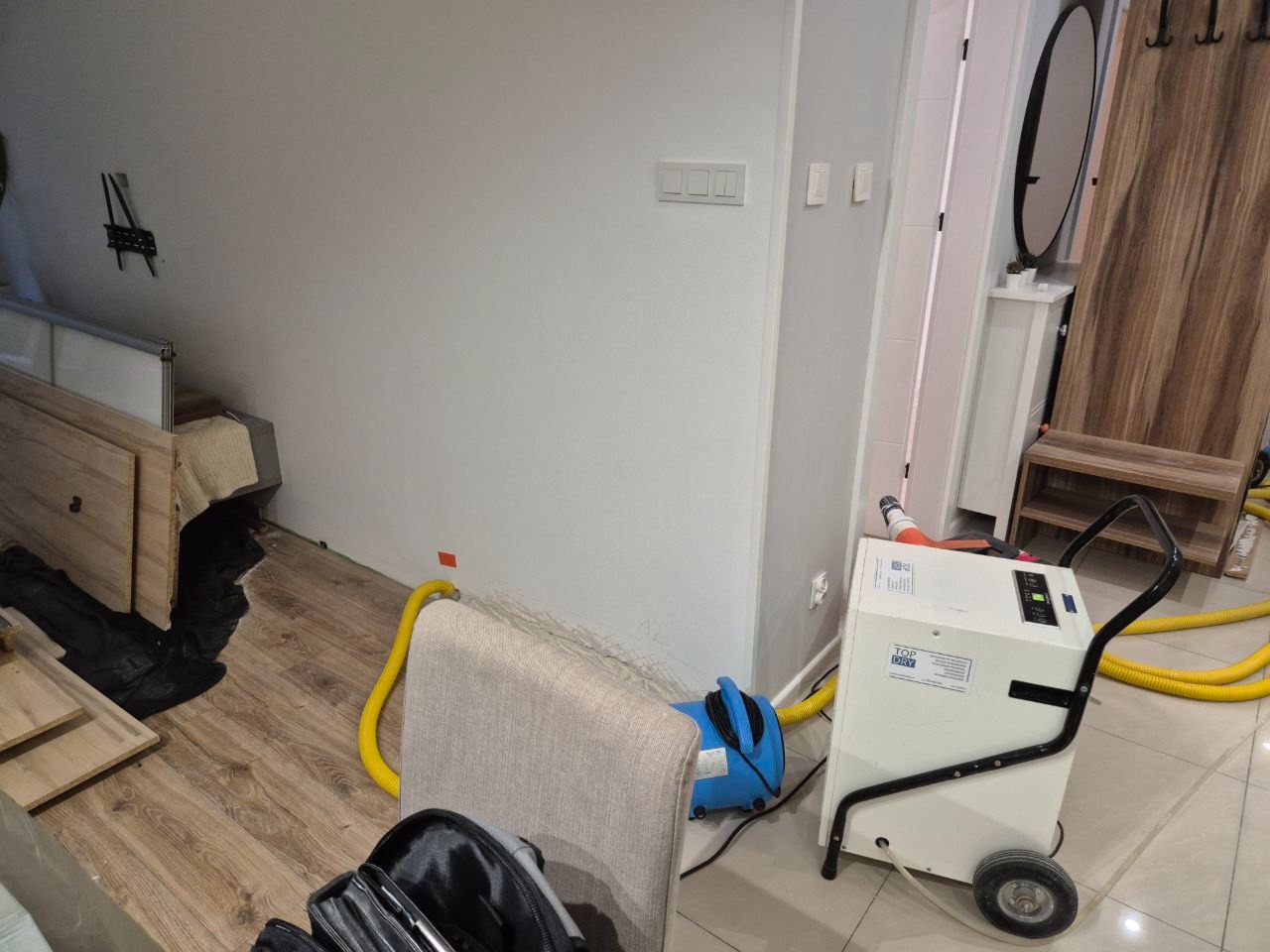 Biały kondensacyjny sprzęt z żółtymi wężami w rogu pokoju podczas pracy. Widoczne meble w trakcie demontażu i przygotowania do procesu.