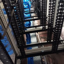 Łukasz Bonikowski ELEKTRO SERWIS - Uporządkowane, niebieskie kable w metalowej szafie serwerowej. Widok z dołu, ukazujący precyzyjne ułożenie przewodów w przestrzeni rackowej.
