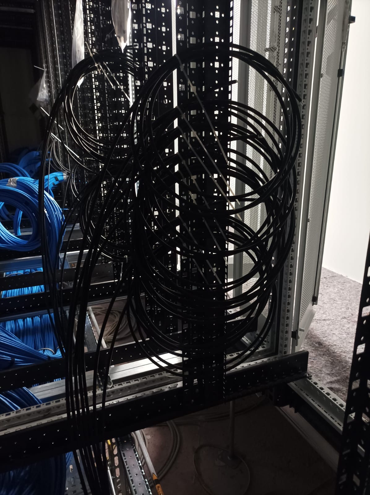 Kłębowisko czarnych kabli w szafie serwerowej, z boku widoczne niebieskie przewody. Elementy metalowe konstrukcji szafy.