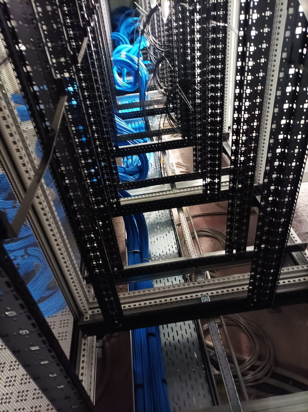 Uporządkowane, niebieskie kable w metalowej szafie serwerowej. Widok z dołu, ukazujący precyzyjne ułożenie przewodów w przestrzeni rackowej.