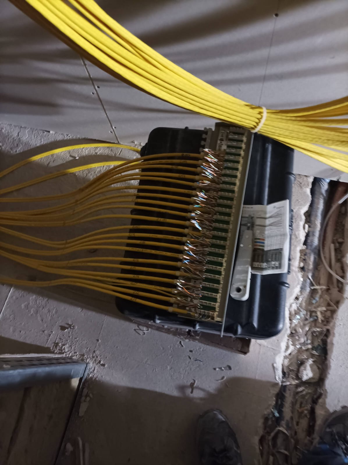 Rozdzielnica elektryczna z podłączonymi przewodami w żółtej izolacji, widoczne złącza i kable. Ujęcie z bliska, instalacja w trakcie prac.