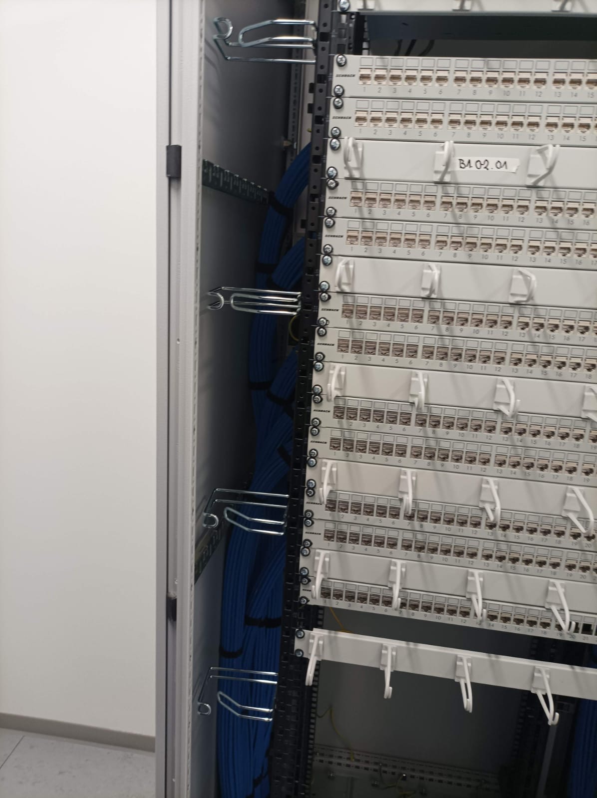 Szafa rack z patch panelem i uporządkowanymi niebieskimi kablami. Widoczne porty z numeracją i uchwyty do zarządzania okablowaniem.