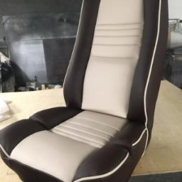 Szafirdesign com - Odnowione, dwukolorowe (brązowo-beżowe) siedzenie samochodowe z wyraźnym przeszyciem i białą lamówką, prezentowane na jasnym tle warsztatowym.