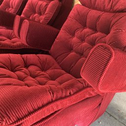 Szafirdesign com - Czerwony, pluszowy fotel z grubym sztruksem, z widocznymi przeszyciami i guzikami, ukazujący detale tapicerki. Widok z bliska na odnowione siedzisko.