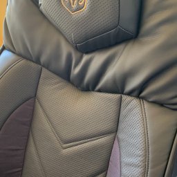 Szafirdesign com - Czarne skórzane siedzenie samochodowe z perforowaną fakturą i wytłoczonym logo w kolorze złotym na zagłówku. Widoczne przeszycia i detale tapicerki.