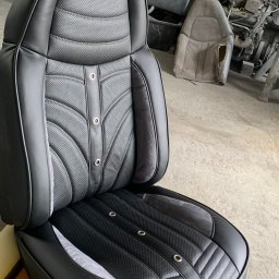 Szafirdesign com - Odnowione czarne skórzane siedzenie samochodowe z perforowaną tapicerką i srebrnymi nitami, widoczne w warsztacie. Detaliczne wykończenie, precyzyjne szwy.