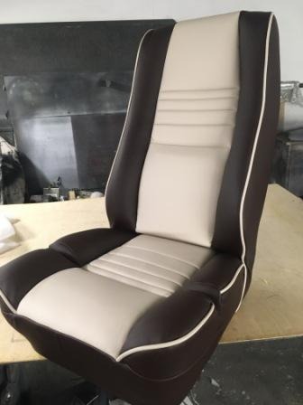 Odnowione, dwukolorowe (brązowo-beżowe) siedzenie samochodowe z wyraźnym przeszyciem i białą lamówką, prezentowane na jasnym tle warsztatowym.