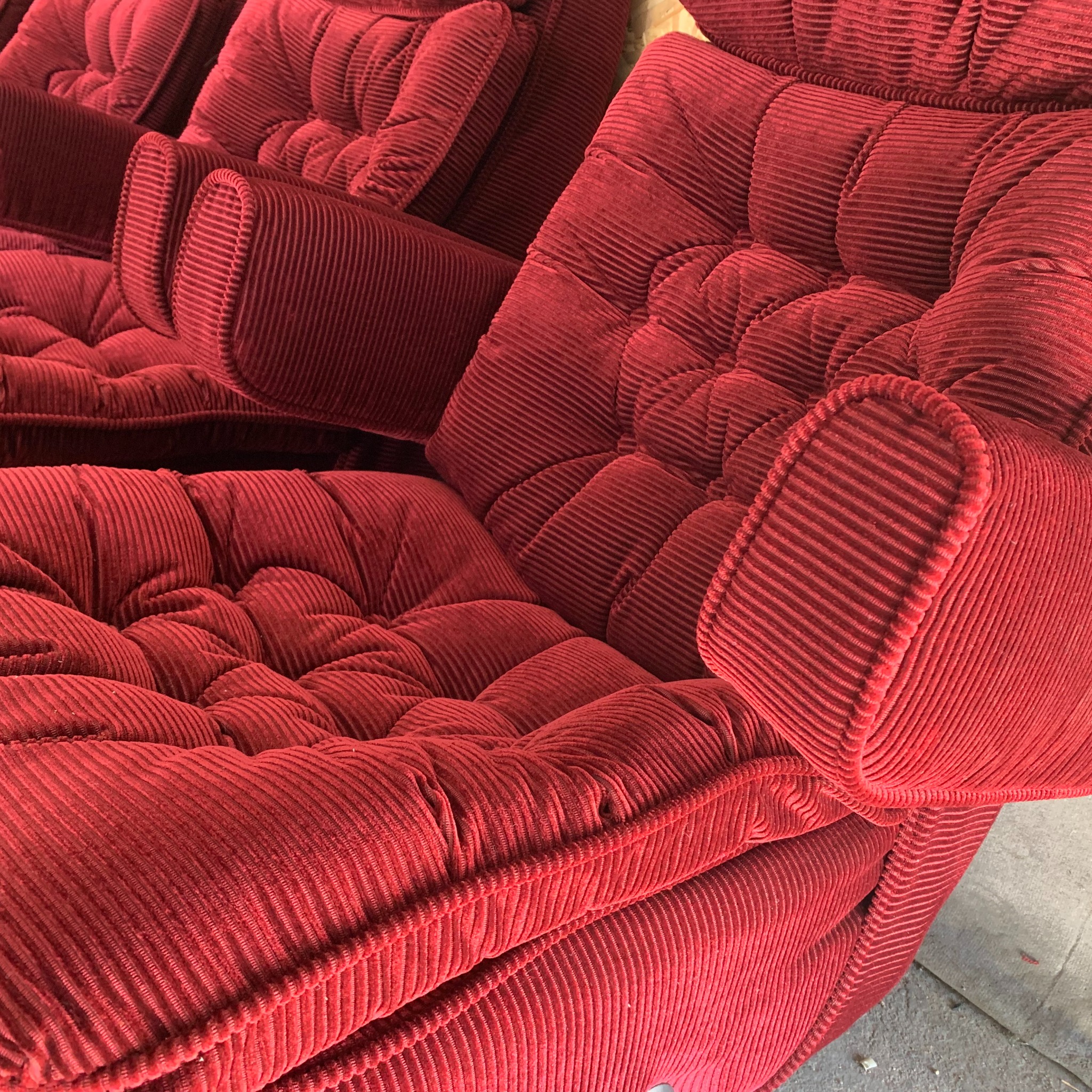 Czerwony, pluszowy fotel z grubym sztruksem, z widocznymi przeszyciami i guzikami, ukazujący detale tapicerki. Widok z bliska na odnowione siedzisko.