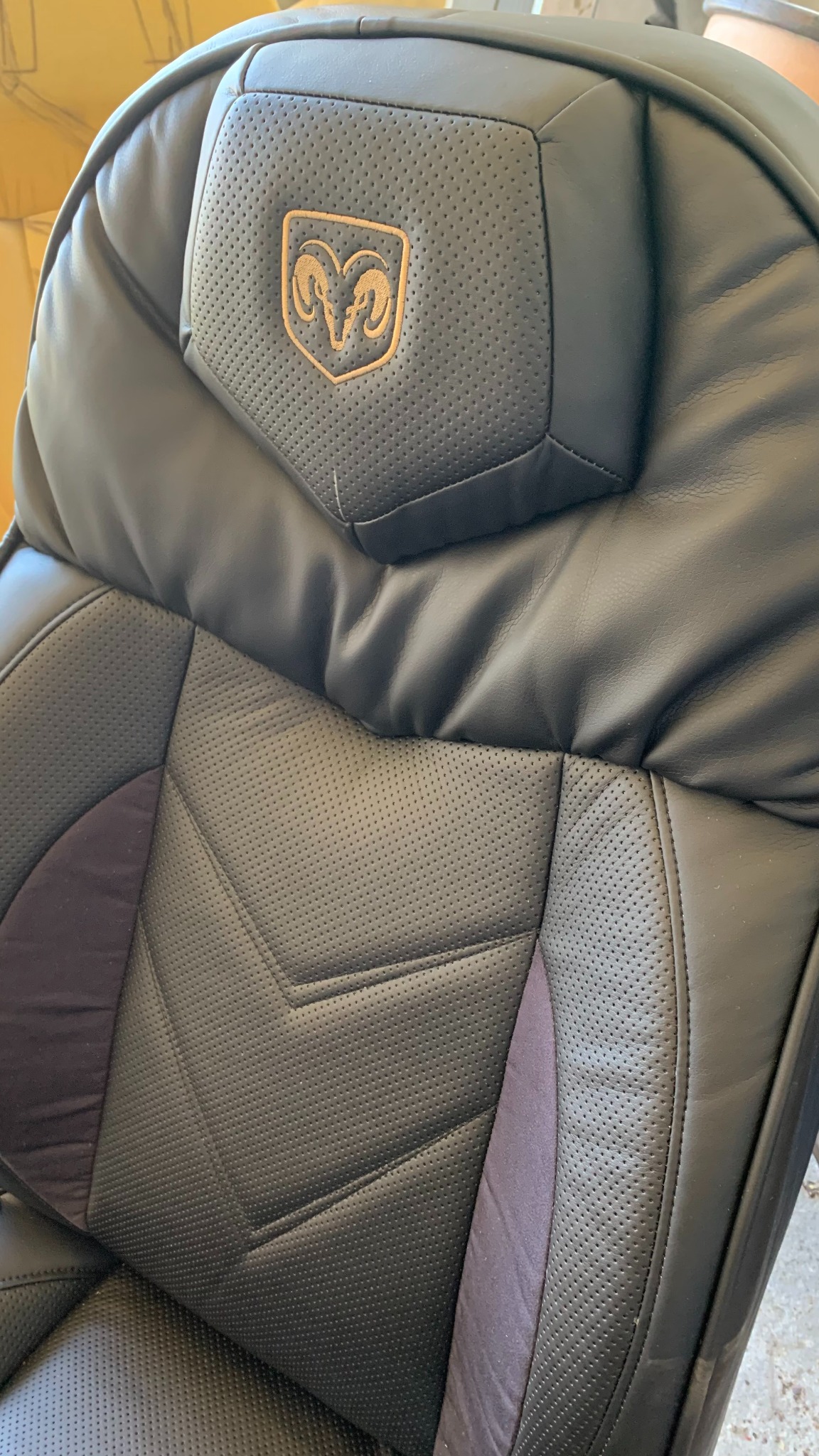 Czarne skórzane siedzenie samochodowe z perforowaną fakturą i wytłoczonym logo w kolorze złotym na zagłówku. Widoczne przeszycia i detale tapicerki.
