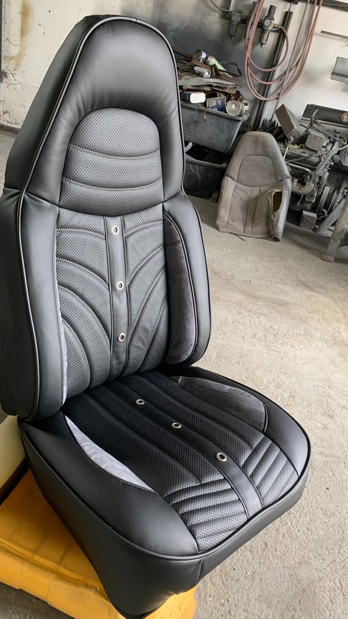 Odnowione czarne skórzane siedzenie samochodowe z perforowaną tapicerką i srebrnymi nitami, widoczne w warsztacie. Detaliczne wykończenie, precyzyjne szwy.