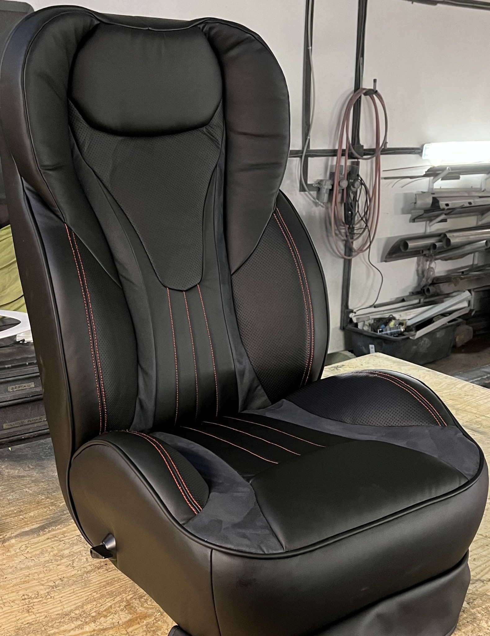 Czarne, skórzane siedzenie samochodowe z czerwoną nicią, prezentowane w warsztacie. Widoczne detale tapicerki i precyzyjne szwy.