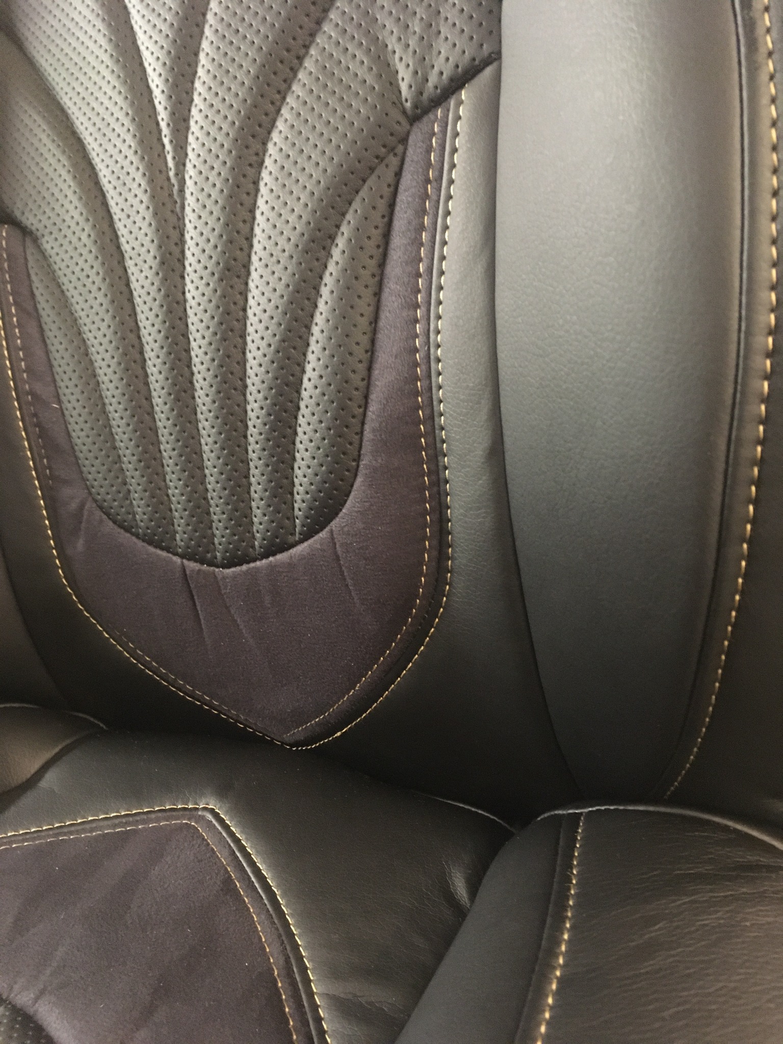 Czarny, skórzany fotel samochodowy z perforowaną wstawką i ozdobnymi przeszyciami w kolorze beżowym. Widoczne detale tapicerki i faktura materiałów.