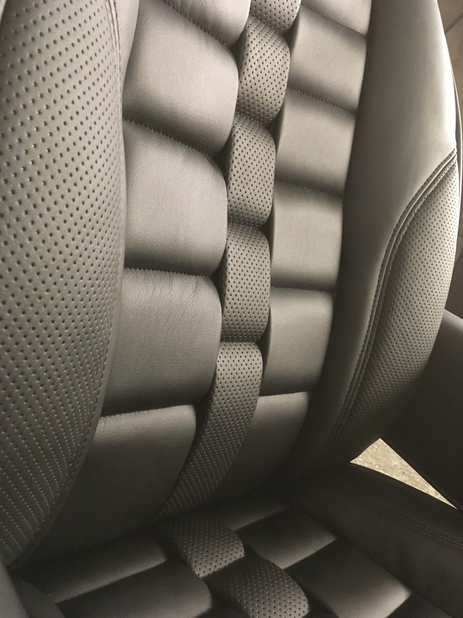 Szare, skórzane obicie fotela samochodowego z perforowanymi elementami i pikowaniem, ukazujące precyzję wykonania i dbałość o detale.