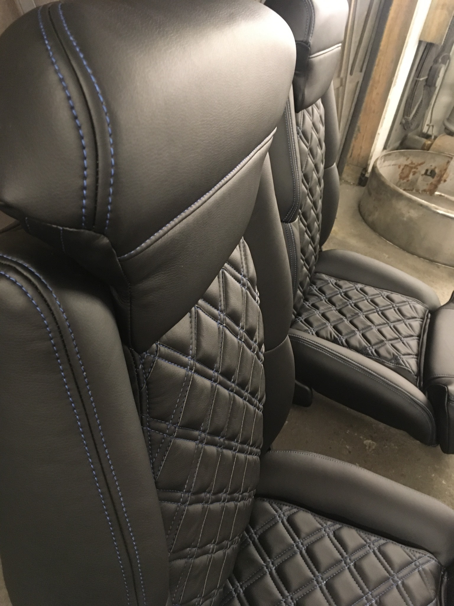 Dwa czarne fotele samochodowe z pikowaną skórą i niebieskimi przeszyciami, ukazane z bliska, prezentujące precyzję wykonania i dbałość o detale tapicerki.