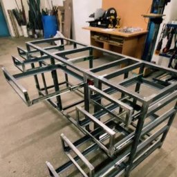 Borys Sanchuk - Szkielet metalowej konstrukcji z wysuwanymi elementami, prawdopodobnie ramy meblowej, w warsztacie z narzędziami w tle. Surowy, industrialny wygląd.