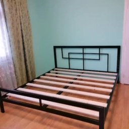 Borys Sanchuk - Czarna, metalowa rama łóżka z drewnianymi listwami na podłodze. Geometryczny wzór wezgłowia. Minimalistyczny design w jasnym wnętrzu.