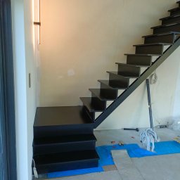 Borys Sanchuk - Nowoczesne, czarne schody metalowe z minimalistyczną balustradą, zamontowane w surowym wnętrzu. Widoczne narzędzia i zabezpieczenia podłogi sugerują etap montażu.