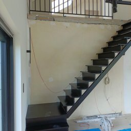 Borys Sanchuk - Ciemne, metalowe schody z balustradą w surowym wnętrzu. Widoczne przewody i niedokończone ściany. Ujęcie z dołu, podkreślające konstrukcję schodów.