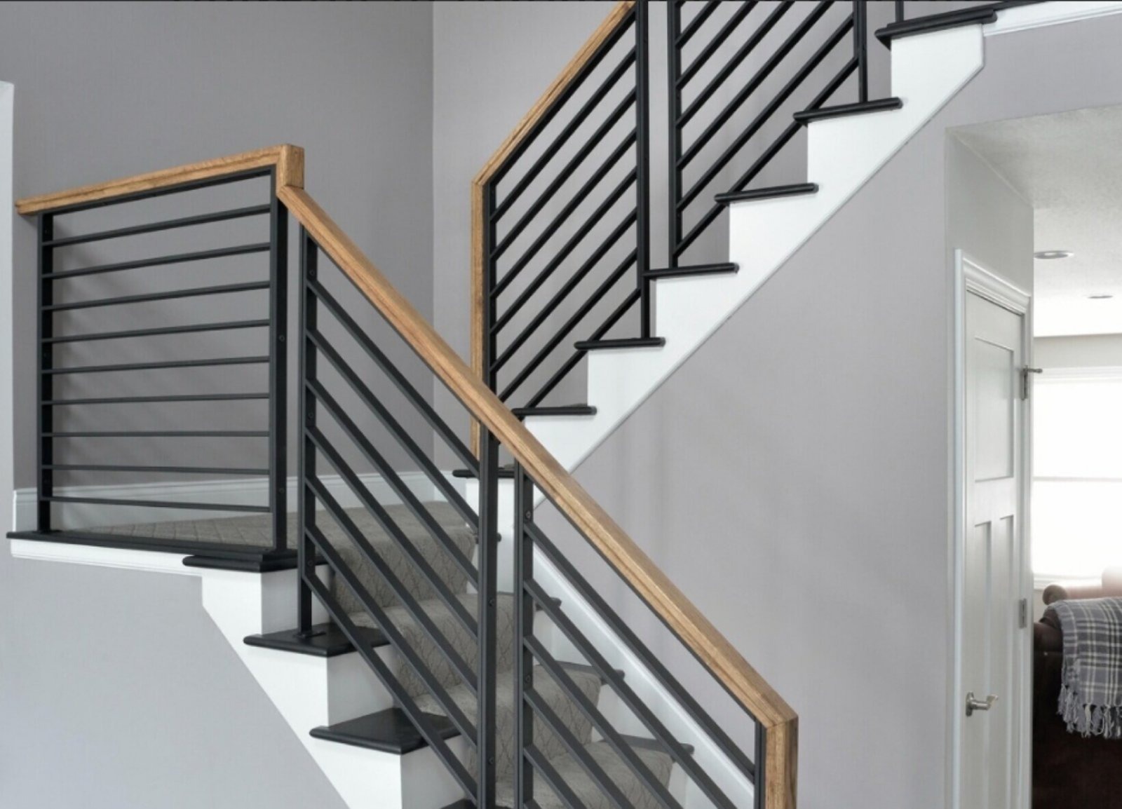 Nowoczesne schody z czarnymi, metalowymi balustradami i drewnianymi poręczami, w jasnym wnętrzu. Minimalistyczny design, poziome pręty, białe stopnie.